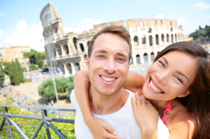 Happy travel couple in piggyback by Coliseum, Rome